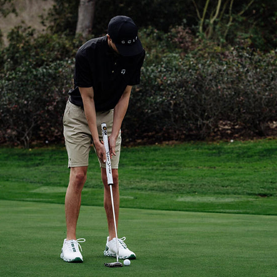 Person playing golf on a green course with trees in the background